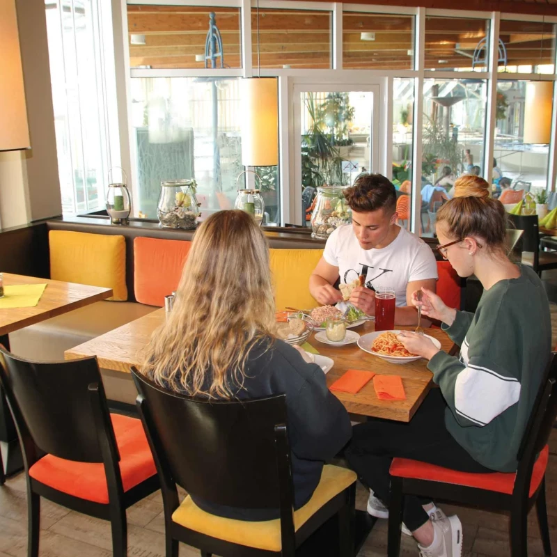 Gruppe junger Menschen beim gemütlichen Mittagessen im Panorama-Bad Restaurant