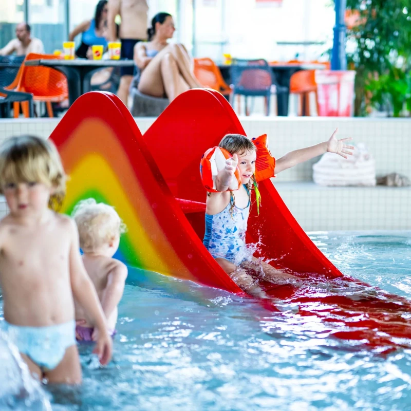 Fröhliche Kinder im Kleinkinderbecken und auf der Regenbogenrutsche um Hintergrund die Bikini-Bar