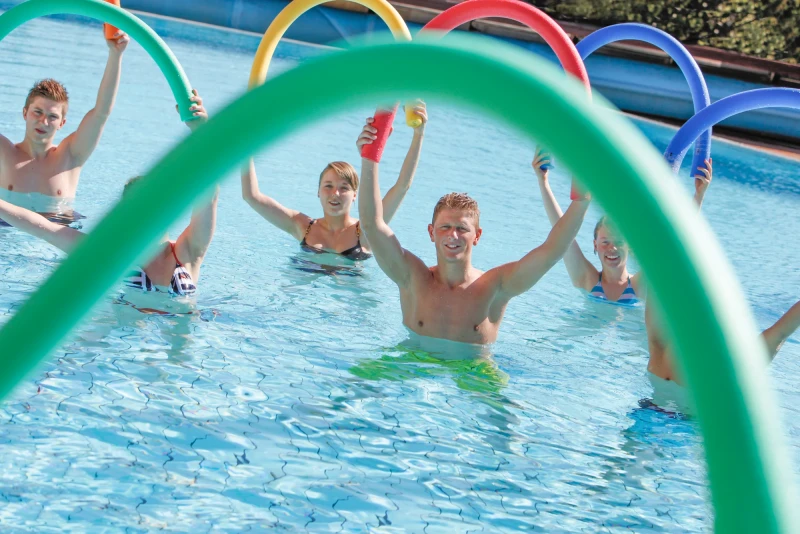 Junge Gruppe beim Aquafitness-Training mit bunten Poolnudeln im Aussenbecken