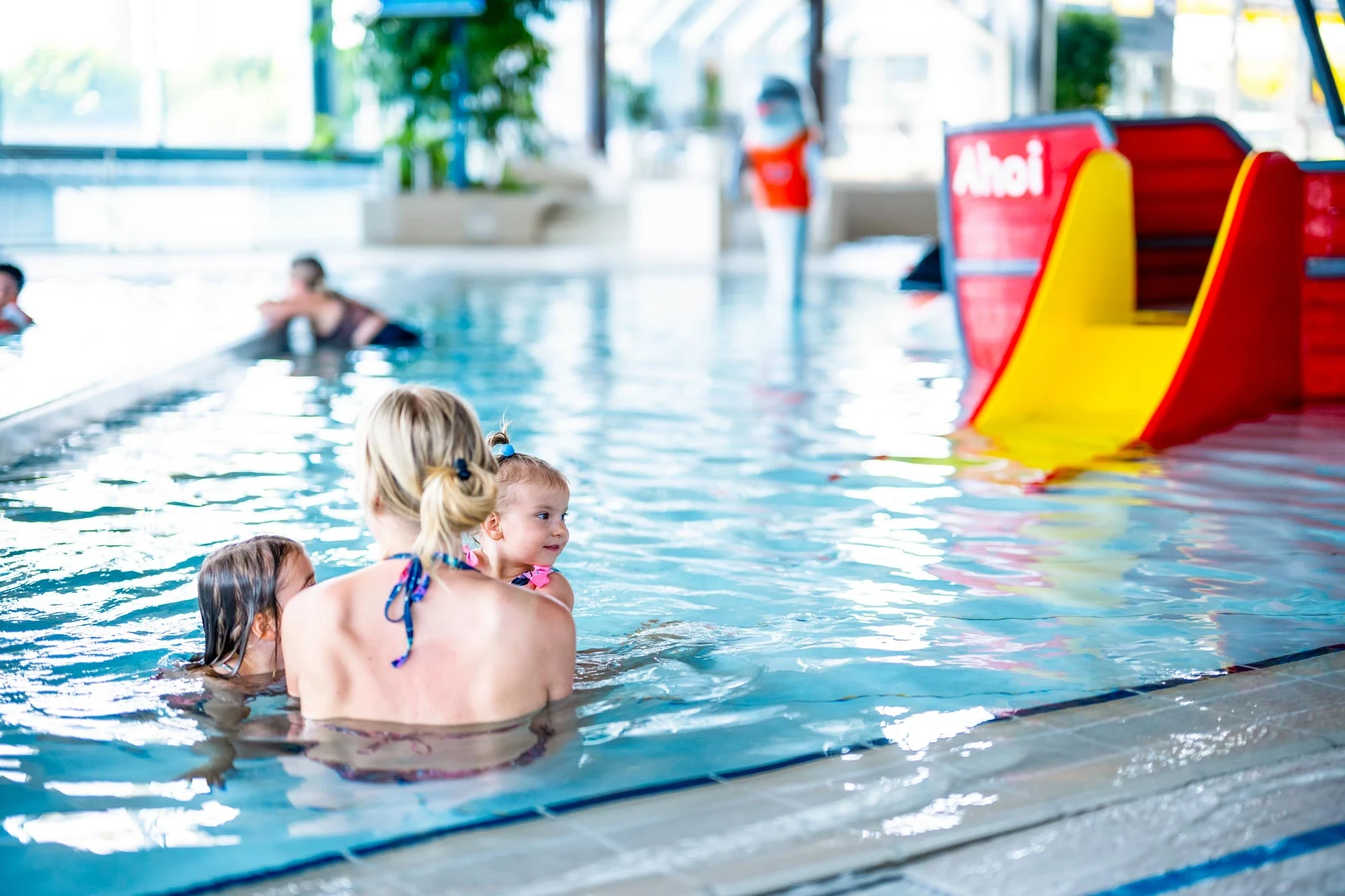 Mutter spielt im Kleinkindbereich mit Ihren zwei Kindern. Im Hintergrund ein Spielschiff mit kleiner Rutsche