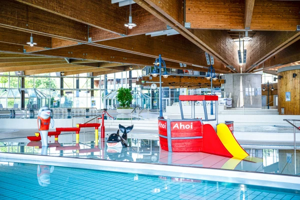 Kleinkinderbecken mit rotem Spielschiff, kleiner Rutsche und verschiedenen Wasserspielzeugen, wie einer Wasserkaskade und einem Reit-Orca