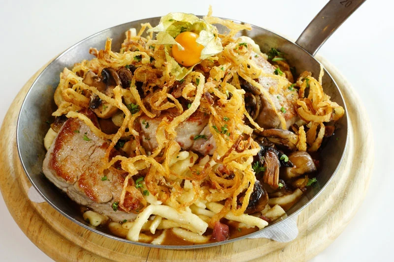 Das Gericht Schwabenpfännle mit Fleisch, Spätzle und Zwiebeln auf Holzbrett