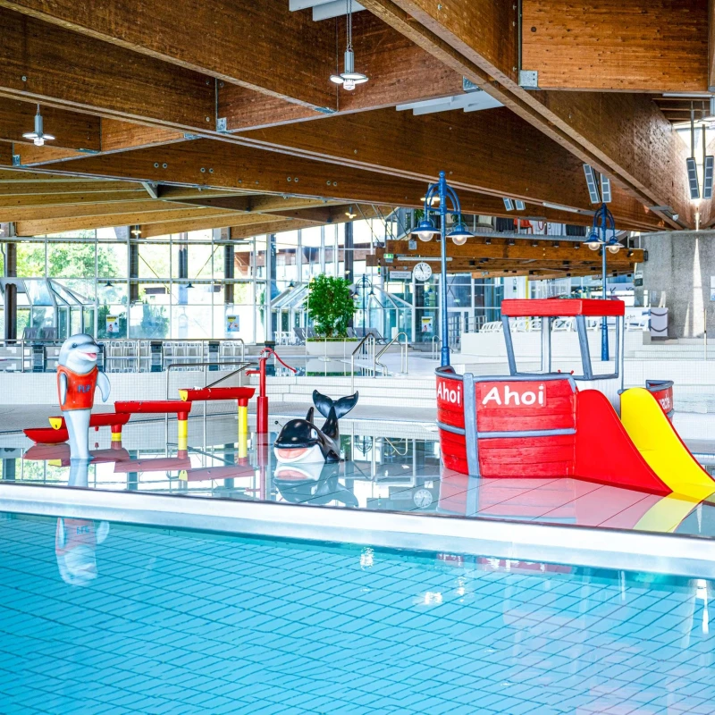Kleinkinderbecken mit rotem Spielschiff, kleiner Rutsche und verschiedenen Wasserspielzeugen, wie einer Wasserkaskade und einem Reit-Orca